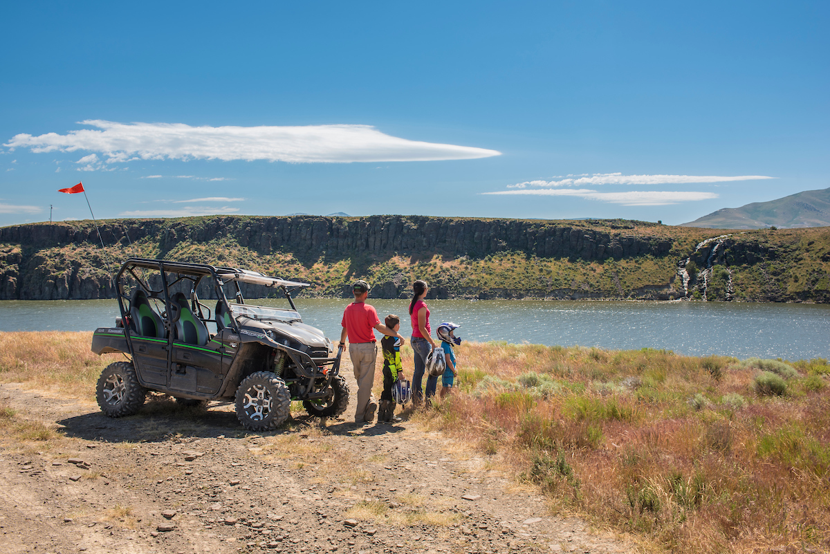 A family of four observes a waterfall across a river as they stand beside an ATV near Oakley in southern Idaho.